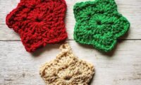Three crochet christmas tree star ornaments in red, green, and tan