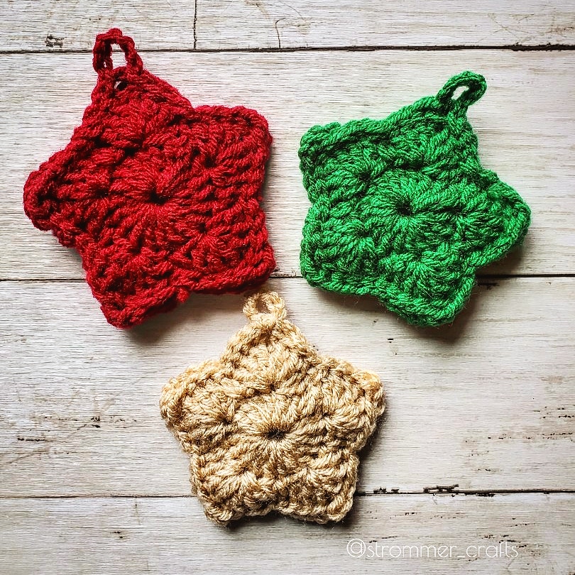 Three crochet christmas tree star ornaments in red, green, and tan